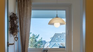 A dining area with a table and chairs, a hanging light fixture, a window with a view of buildings, and a radiator.