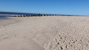 A wide sandy beach with footprints and a row of large boulders in the distance.