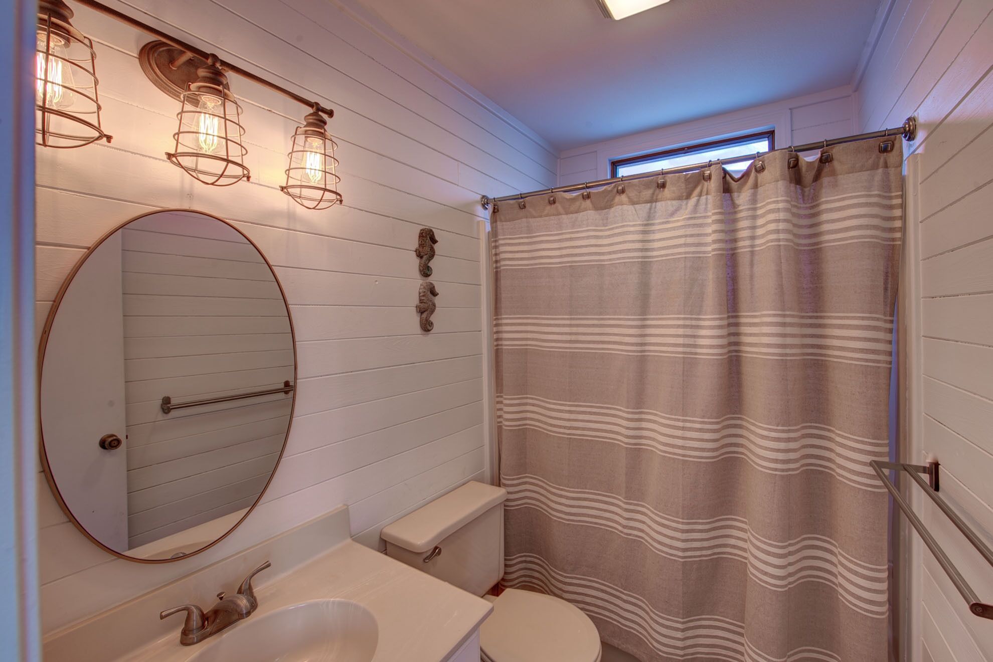 A bathroom with a round mirror, a sink, a toilet, and a shower curtain.