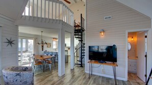 A spacious living area with a dining table, chairs, a TV, and a staircase leading to an upper level. - Semi-Oceanfront home with direct access to the beach! (Avon)