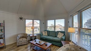 A cozy living room with a wooden floor, a green sofa, a patterned armchair, a wooden coffee table, and a bookshelf. - Semi-Oceanfront home with direct access to the beach! (Avon)