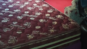 Ein Schlafzimmer mit einem Bett, einem roten Sofa, einem gemusterten Teppich und einem Fenster mit Jalousien.