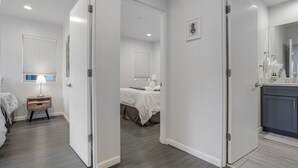 Habitación de hotel con cama, mesita de noche, lámpara y baño con espejo y perchero.