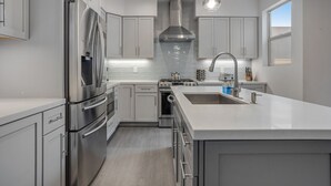 Cocina moderna con electrodomésticos de acero inoxidable, muebles grises e iluminación colgante.