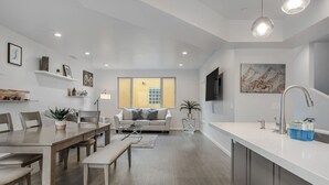 Una sala de estar moderna con comedor, una cocina con una isla grande y vistas al exterior a través de un ventanal.