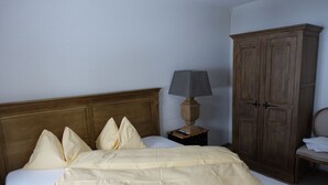 Ein ordentlich bezogenes Bett mit Holz-Kopfteil, einer Nachttischlampe und einem Kleiderschrank.