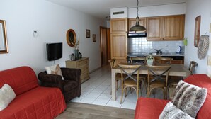 Ein Wohnzimmer mit rotem Sofa und braunem Sessel, ein Essbereich mit Holzsesseln und Tisch, sowie eine Küche mit Holdekor-Schränken und Herd.