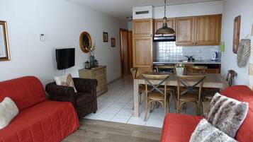 Ein Wohnzimmer mit rotem Sofa und braunem Sessel, ein Essbereich mit Holzsesseln und Tisch, sowie eine Küche mit Holdekor-Schränken und Herd.