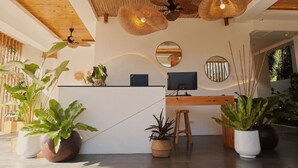A reception area with a wooden desk, two monitors, and a mirror. There are several potted plants and a ceiling fan. - Molly Resort Bohol (Panglao)