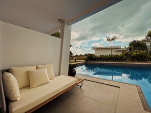 Un espacio moderno al aire libre con piscina, una pared blanca y vistas a una casa y palmeras.