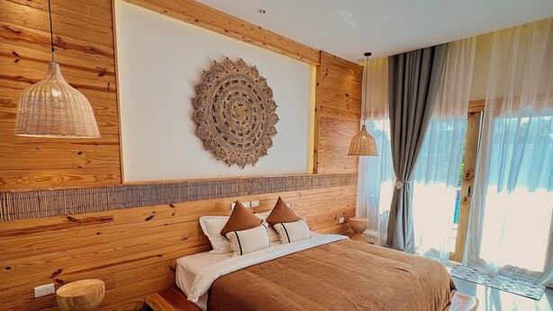 A modern bedroom with a wooden headboard, a large circular wall decoration, a bed with a brown blanket, and a round rug. - Molly Resort Bohol (Panglao)