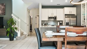Une cuisine moderne avec des meubles blancs, des appareils en acier inoxydable et un coin repas comprenant une table et des chaises en bois.