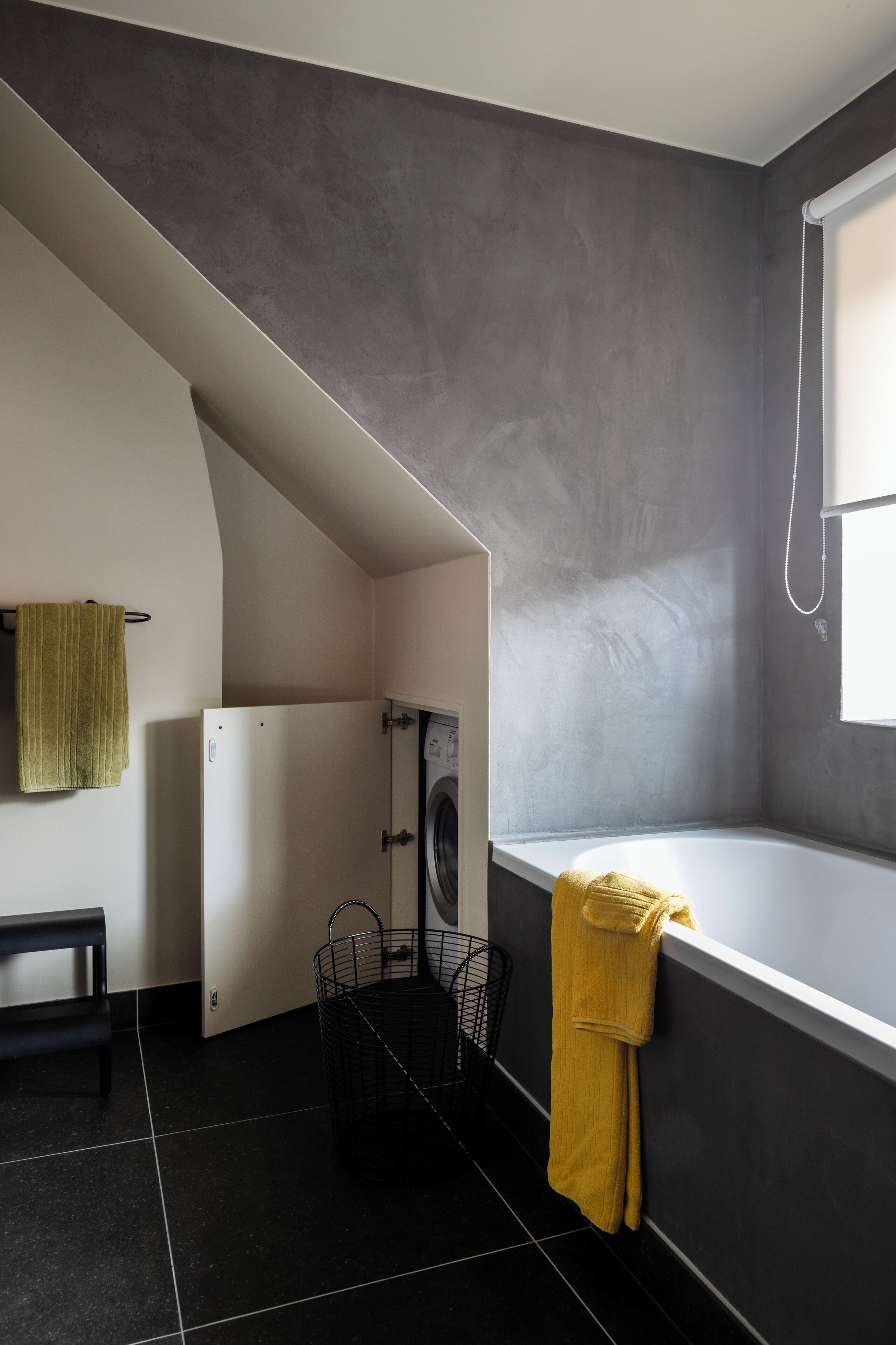 A compact bathroom with a bathtub, a towel rack, and a laundry basket.