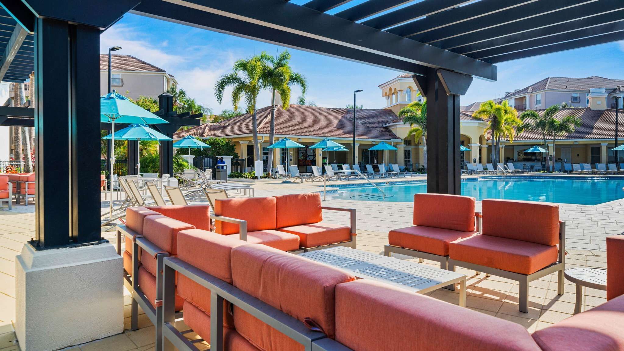 A poolside area with lounge chairs and umbrellas, a pool, and buildings in the background.