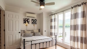 Een slaapkamer met een bed, een plafondventilator, een raam met gordijnen en kunst aan de muur.