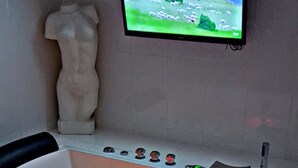 Ett spa-rum med en massagebänk, en tv som är monterad på väggen och en dekorativ staty.