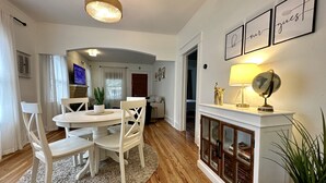 Un comedor con una mesa redonda, sillas blancas, un tapete, una chimenea con una lámpara y cuadros en la pared.