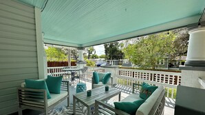 Un patio techado al aire libre con muebles blancos, un tapete estampado y vistas del vecindario.