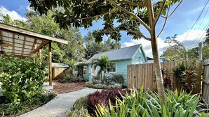Un jardín con un sendero de grava que lleva a una casa con techo azul y valla de madera.