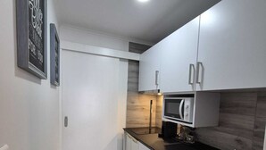 Una cocina compacta con armarios blancos, una encimera negra, un lavamanos de acero inoxidable y un microondas.