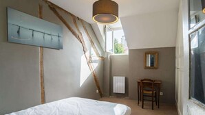 Een slaapkamer met een bed, een stoel, een bureau, een radiator en een raam.