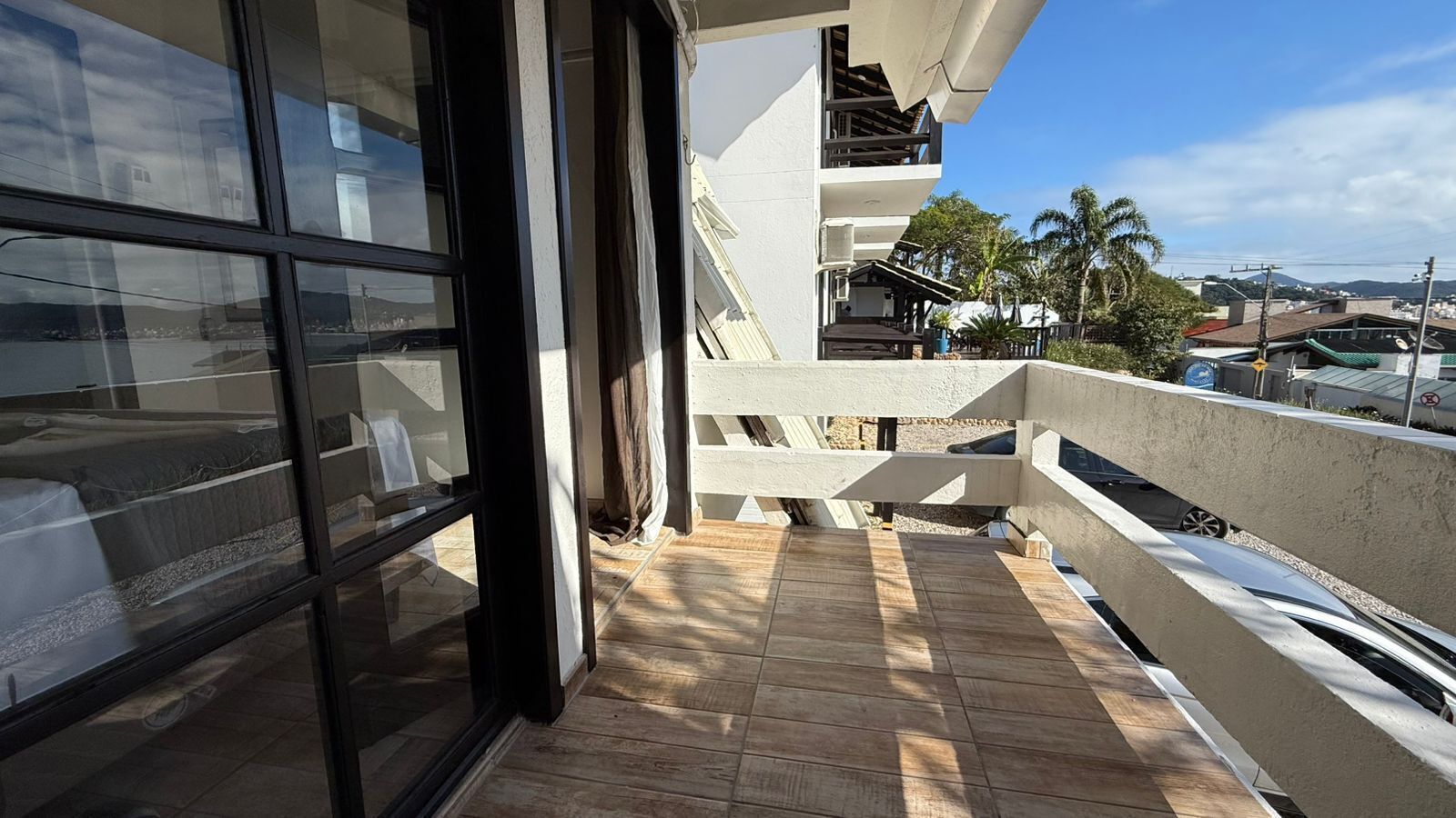 A balcony with a view of the city, a wooden floor, and a glass door leading to a room.