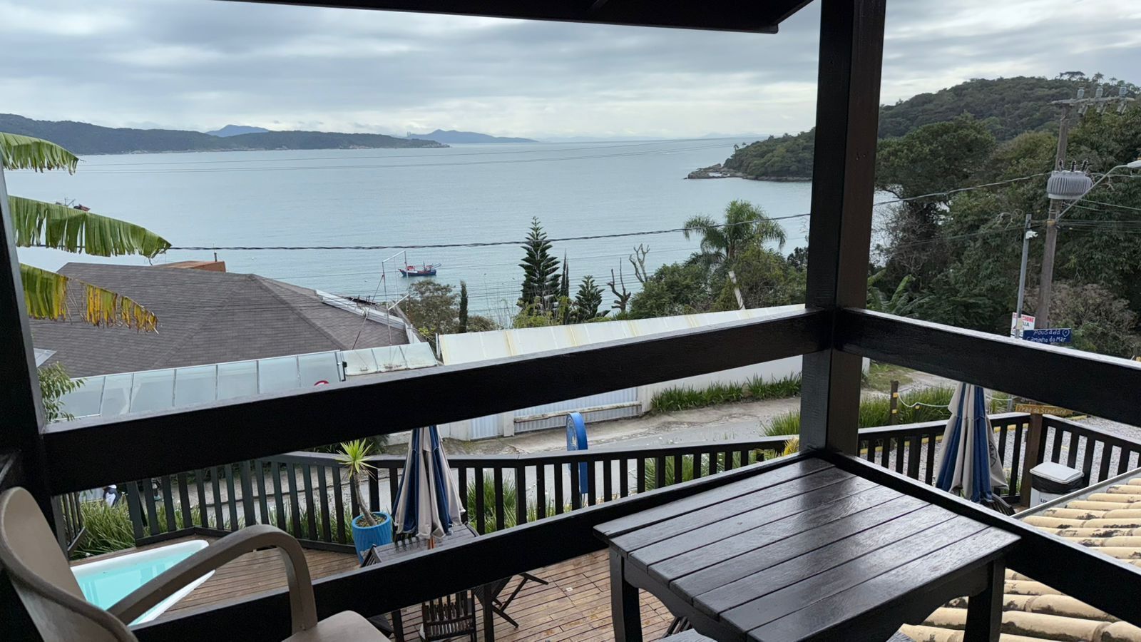 A balcony with a view of the sea, a chair, a small table, and a potted plant.