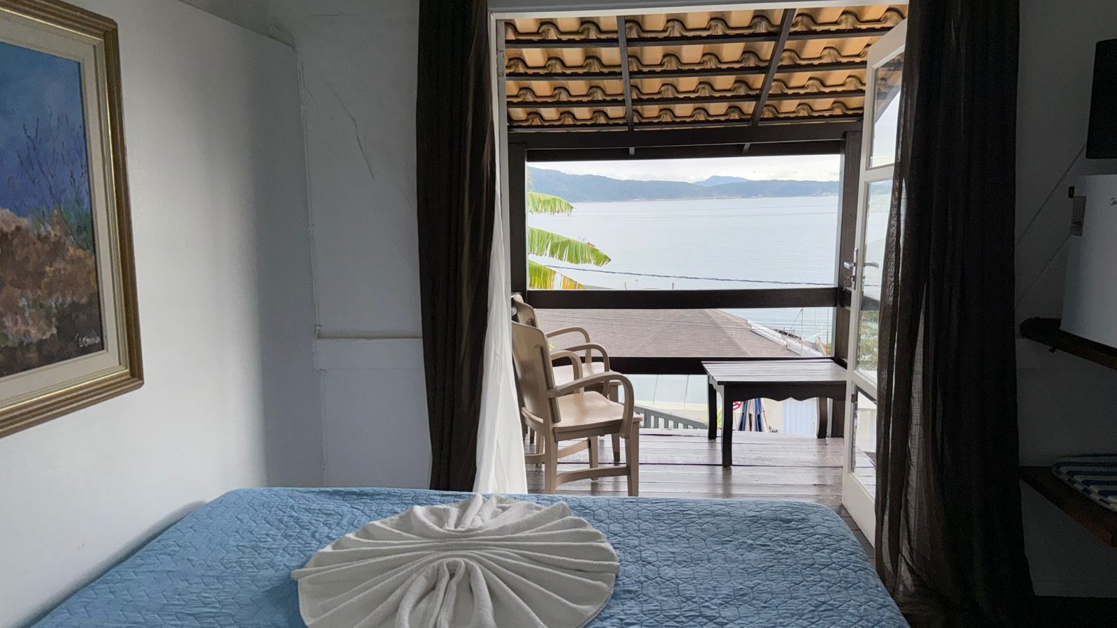 A room with a bed, a table, and a view of the sea.