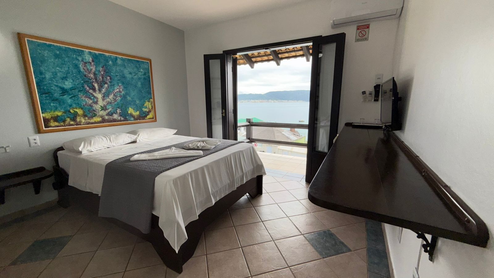 A bedroom with a bed, a painting, a window, and a TV.