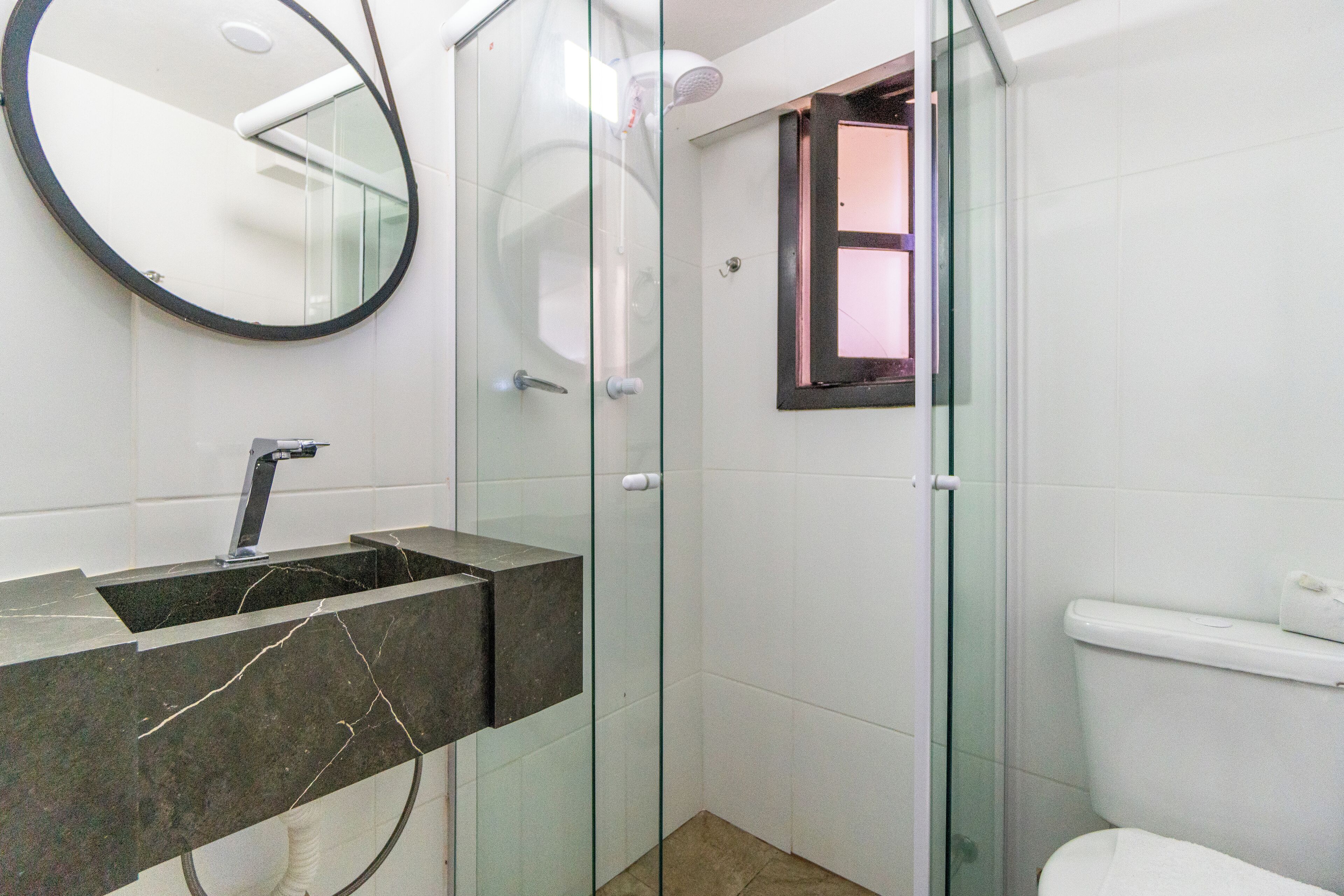 Un baño moderno con ducha envuelta en vidrio, lavamanos de mármol y un inodoro.