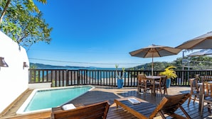 Una terraza de madera con piscina, mobiliario exterior y vistas al mar.