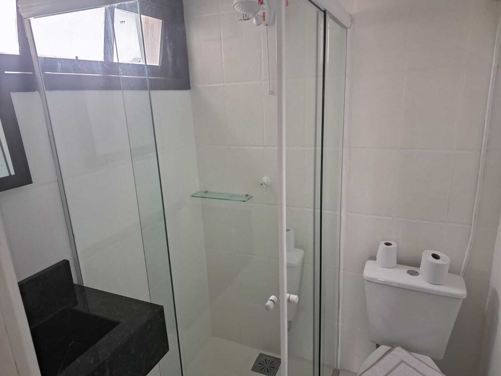 Une salle de bain avec une douche à parois de verre, une étagère en verre et des toilettes avec deux rouleaux de papier toilette.