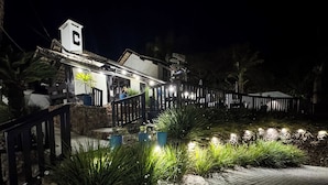 Un edificio de fachada de piedra, un letrero con una 'C' y una entrada bien iluminada con una valla de madera.