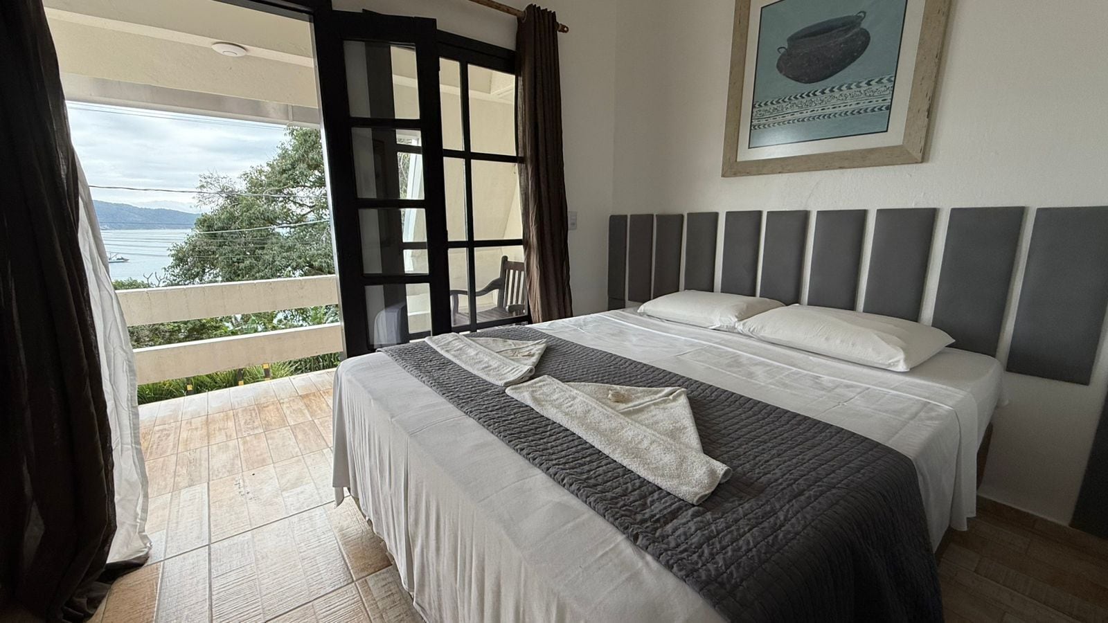 A bedroom with a bed, a view of the outdoors, and a framed picture on the wall.