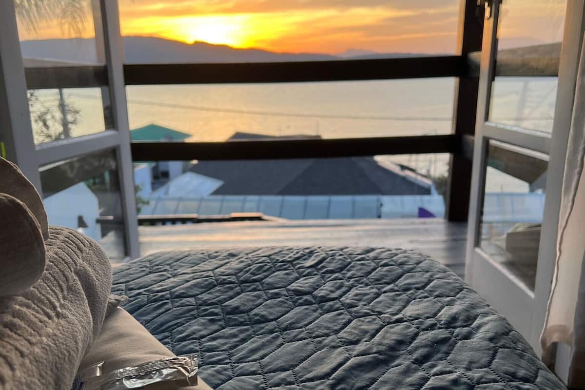 A bed with a quilted blue cover, a beige pillow, and a small bag on it.