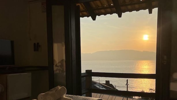 Una habitación con cama, televisor y vistas a la puesta de sol sobre el agua.