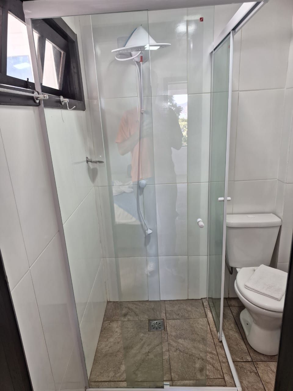 Un box de ducha con paredes de vidrio, un inodoro blanco y una ventana arriba.