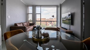 A modern living room with a glass table, leather sofa, and a TV on the wall. - Sandton Smart Apartment Fifteen (Sandton)