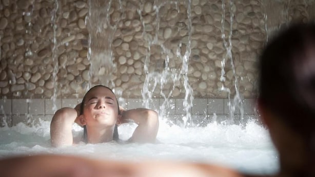 Una persona relajándose en un jacuzzi con agua cayendo de una pared de piedra.