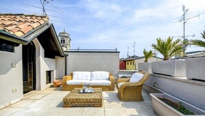 Un patio en la azotea con un sofá blanco, sillas de mimbre y una pequeña mesa.
