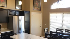 A kitchen with dark cabinets, a stainless steel refrigerator, a marble countertop, and a dining area with wooden chairs and a table. - Lavender Lane (Phoenix)