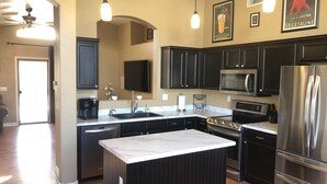 A modern kitchen with dark cabinetry, a stainless steel refrigerator, a built-in oven, and a large island with a marble countertop. - Lavender Lane (Phoenix)