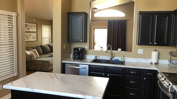 A modern kitchen with dark cabinetry, a marble countertop, a built-in dishwasher, and a stove. - Lavender Lane (Phoenix)