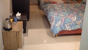 A bedroom with two beds, a bedside table with a kettle and tissues, and a wooden cabinet. - Ali Jasem Group (Doha)