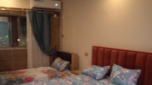 A bedroom with a red headboard, floral bedding, and a window with curtains. - Ali Jasem Group (Doha)
