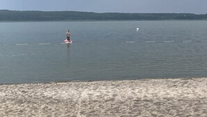 Een strand met iemand in het water, een zandstrand en een verre horizon.