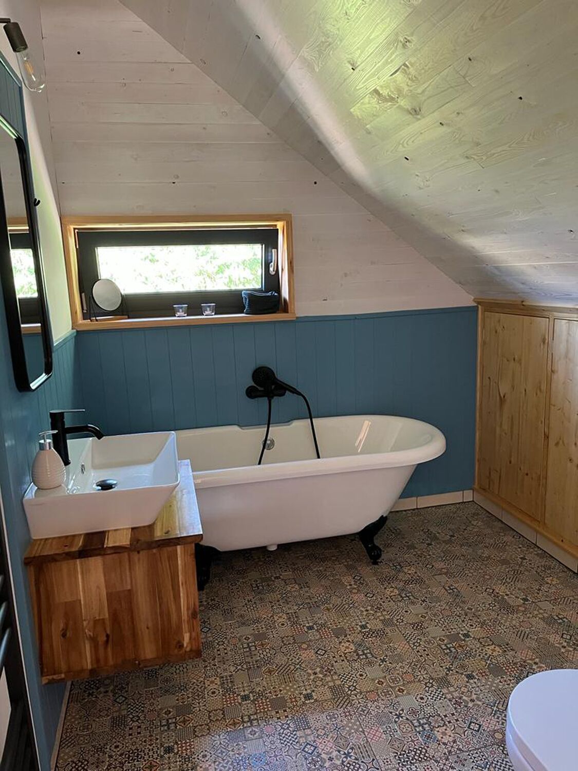 A bathroom with a freestanding bathtub, a wooden vanity, a sink, and a window above the bathtub.