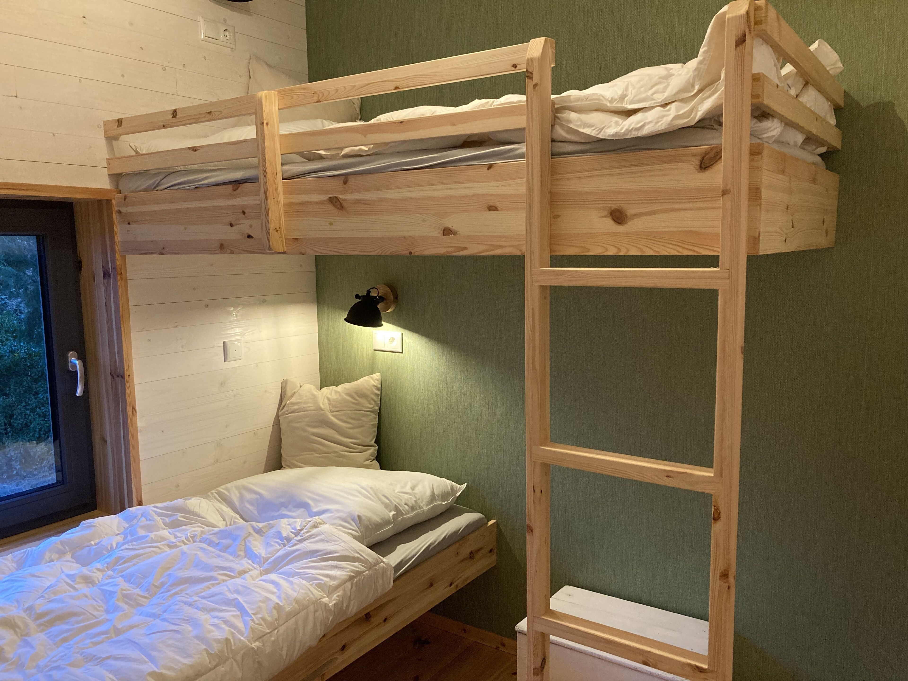 Un lit superposé avec une échelle, une table de chevet et une lampe fixée au mur.