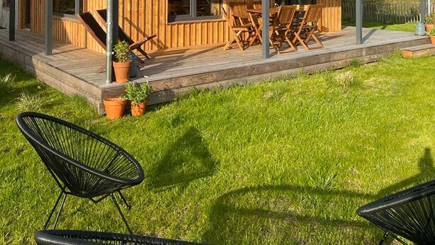 Een modern houten huis met een overdekte veranda, grote ramen en buitenmeubels.