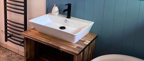 Een badkamer met een wit wastafel, een zwarte kraan en een spiegel erboven. Links een handdoekhouder en rechts een bad.